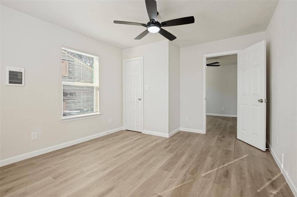 Neutral-toned room featuring wood-finish flooring, a ceiling fan with integrated lighting, and a six-panel door