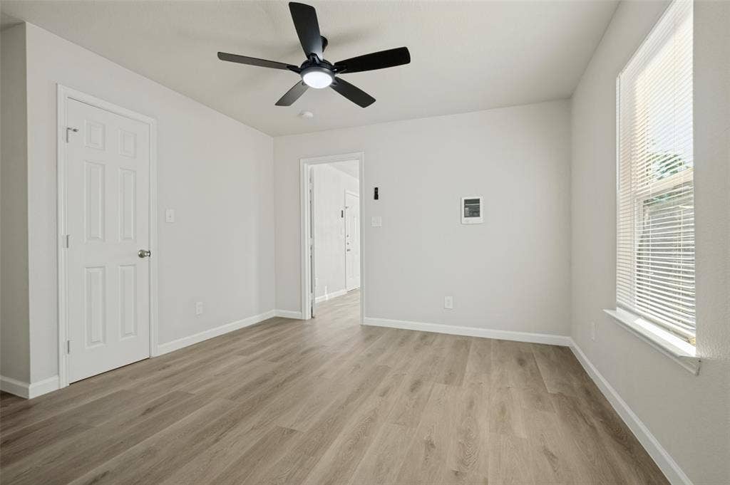 Neutral interior space featuring wood-finish flooring, a ceiling fan with integrated lighting, and a window with horizontal blinds