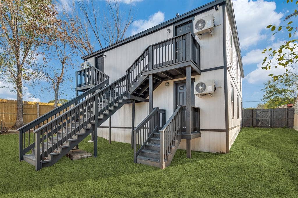Exterior featuring vertical panel siding, dark-finished wood staircases with railings, multiple entry points, and fenced perimeter