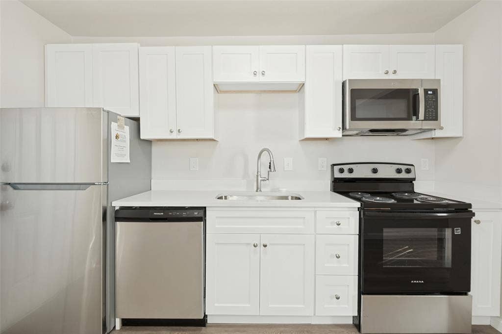 Kitchen featuring white shaker-style cabinetry, solid-surface countertops, stainless steel appliances, and a gooseneck faucet