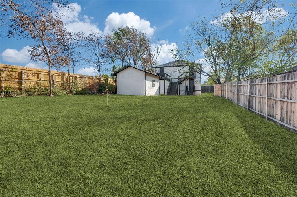 Expansive backyard featuring a level lawn, mature trees, and wood privacy fencing, complete with a detached storage structure
