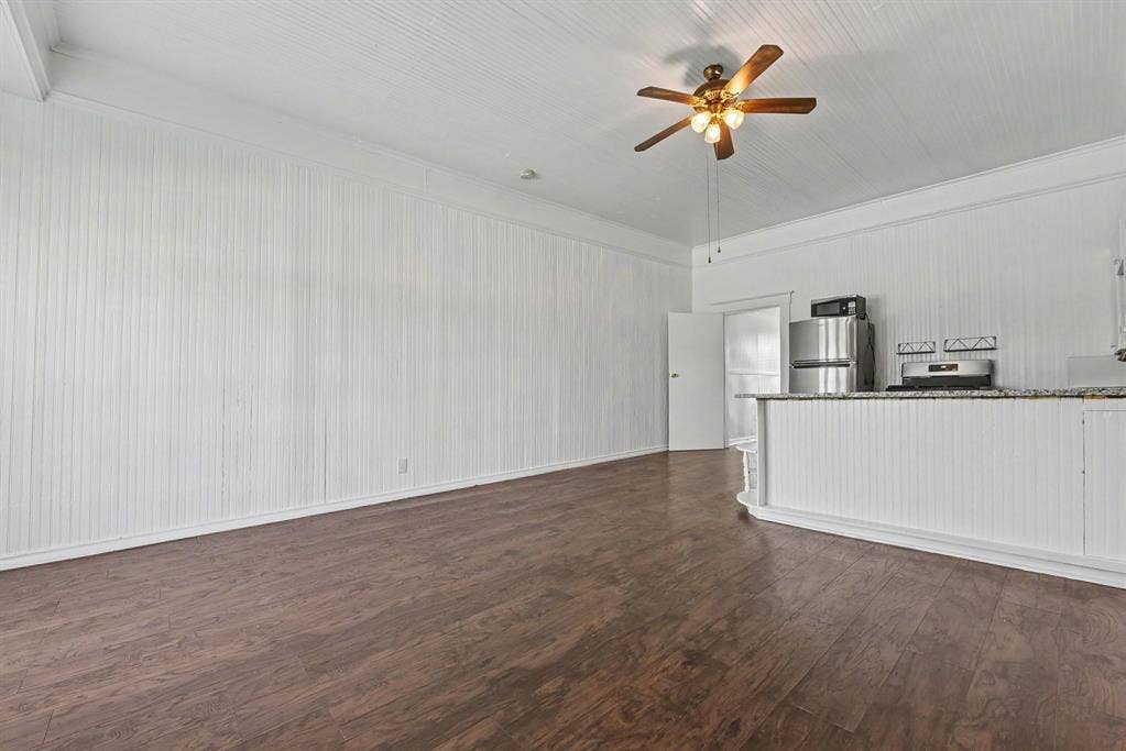 105 College Street, #107, Wylie, TX 75098 Beadboard wall paneling, wood-finish flooring, white beadboard ceiling, ceiling fan with integrated lighting, and kitchen peninsula with stone-finish countertop