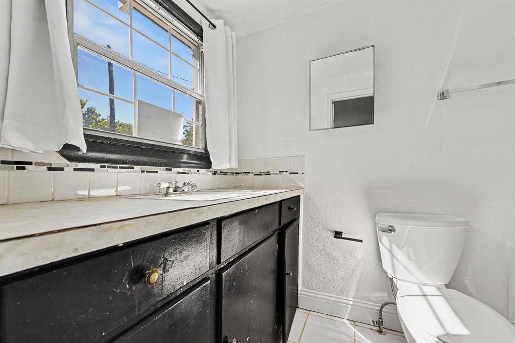 105 College Street, #107, Wylie, TX 75098 Vanity featuring stone-surfaced countertop, integrated basin, and dark-finished cabinetry, accented by multi-toned mosaic tile backsplash, rectangular wall-mounted mirror, and tile flooring