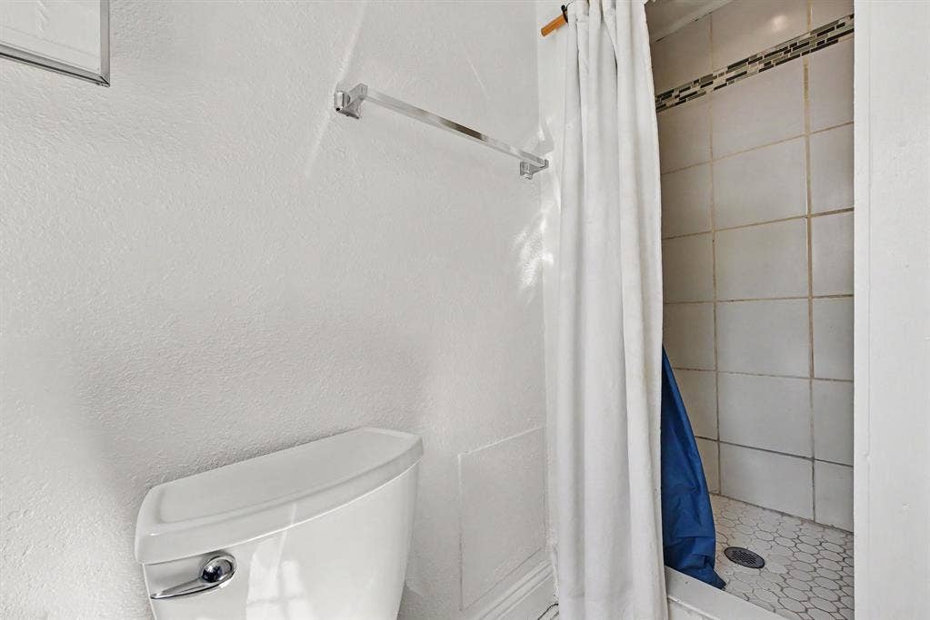 105 College Street, #107, Wylie, TX 75098 Bathroom featuring a white ceramic toilet, chrome towel bar, walk-in shower with square wall tile, mosaic floor tiling, and a decorative tile accent border