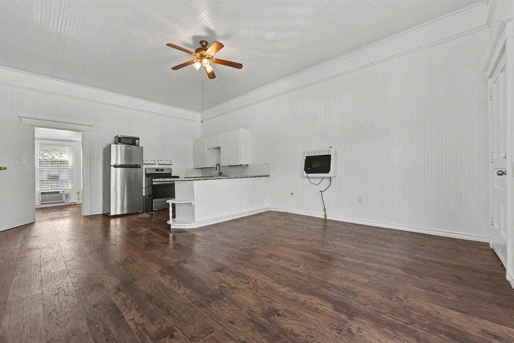 105 College Street, #107, Wylie, TX 75098 Interior featuring beadboard walls, wood-finish flooring, high ceilings, a ceiling fan, and a kitchen with white cabinetry and a breakfast bar