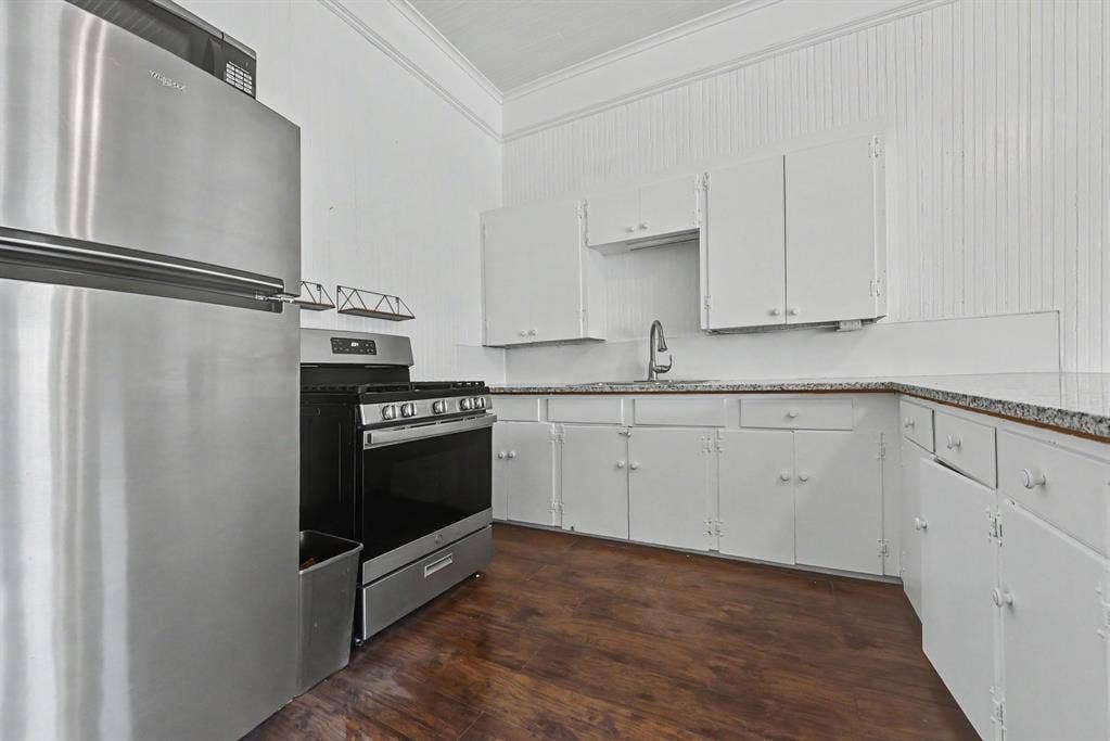 105 College Street, #107, Wylie, TX 75098 Kitchen featuring stainless steel appliances, wood-finish flooring, white cabinetry, beadboard wall paneling, and stone-surfaced countertops