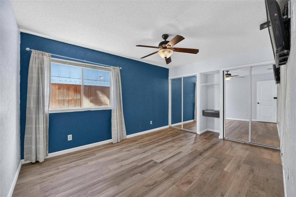 2130 Bowie Drive, Carrollton, TX 75006 Wood-finish flooring, accent wall, ceiling fan with light fixture, and floor-to-ceiling sliding mirror closet doors
