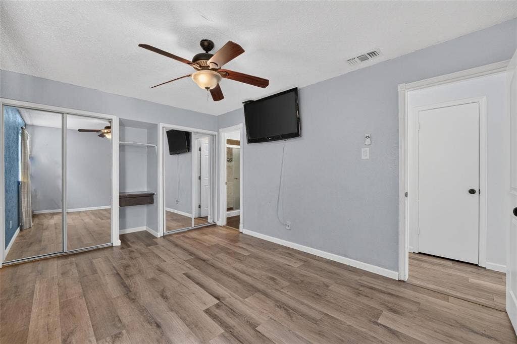 2130 Bowie Drive, Carrollton, TX 75006 Wood-finish flooring, dual sliding mirrored closet doors, built-in shelving, and a ceiling fan with integrated light fixture