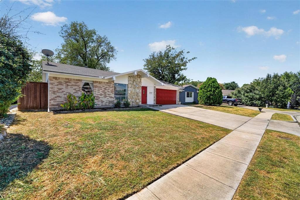 2130 Bowie Drive, Carrollton, TX 75006 Single-story exterior featuring a brick and stone facade, a concrete driveway, a prominent red front door, and a wood privacy fence