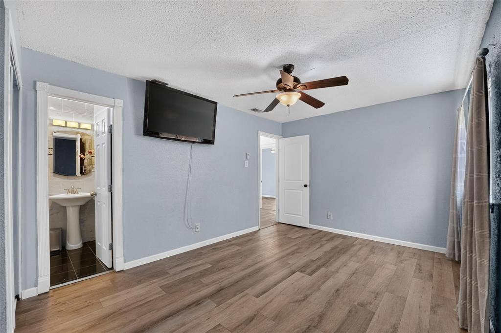 2130 Bowie Drive, Carrollton, TX 75006 Room featuring wood-finish flooring, a ceiling fan with integrated lighting, and a doorway revealing a pedestal sink