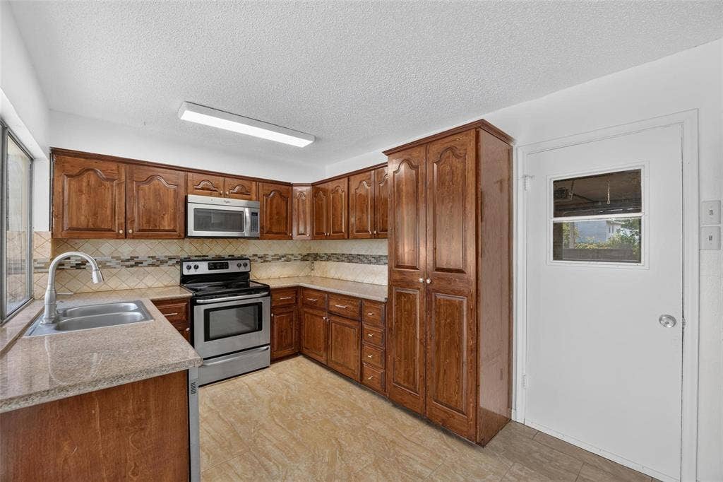 2130 Bowie Drive, Carrollton, TX 75006 Kitchen featuring wood cabinetry, stone-finish countertops, stainless steel appliances, tiled backsplash, and recessed overhead lighting