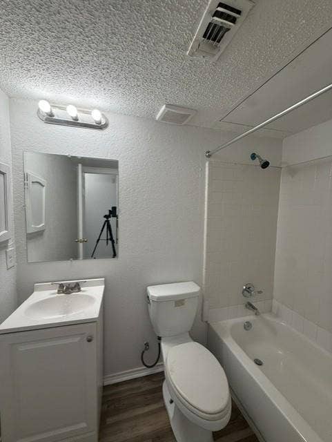 Bathroom featuring a white vanity cabinet with a integrated sink, three-bulb vanity lighting, a wall-mounted mirror, wood-finish flooring, and a tub with tiled surround