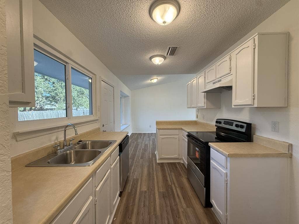 Kitchen featuring white cabinetry, wood-finish flooring, dual-basin stainless steel sink, and a range with overhead range hood