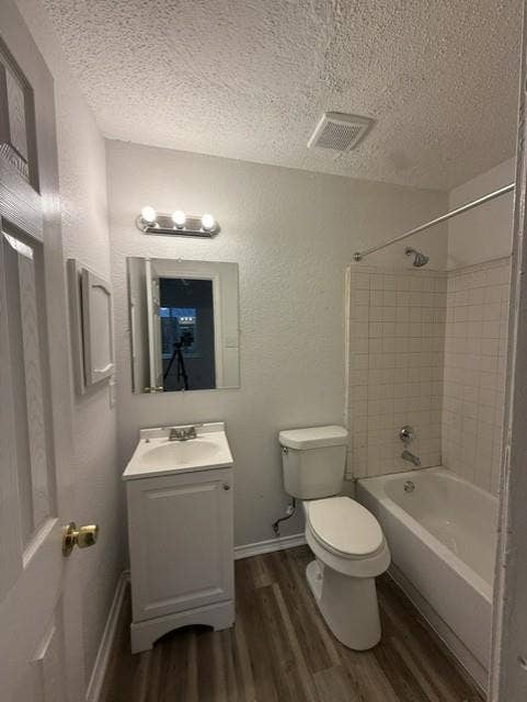 Bathroom featuring a vanity with an integrated sink, wood-finish flooring, a wall-mounted vanity light fixture, and a tile-surround shower and tub combination