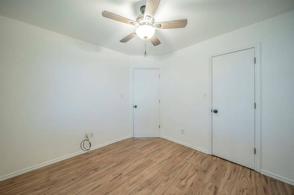Neutral interior featuring wood-finish flooring, a ceiling fan with integrated lighting, and two interior doors with matte black hardware