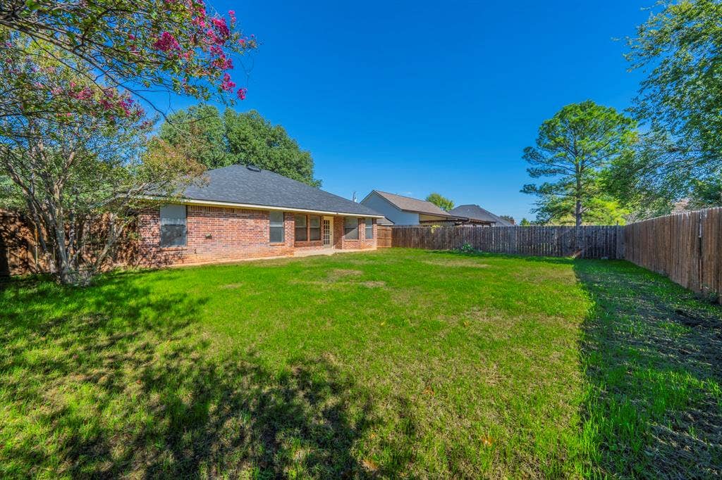 Expansive backyard featuring a brick exterior, privacy wood fencing, and mature landscaping