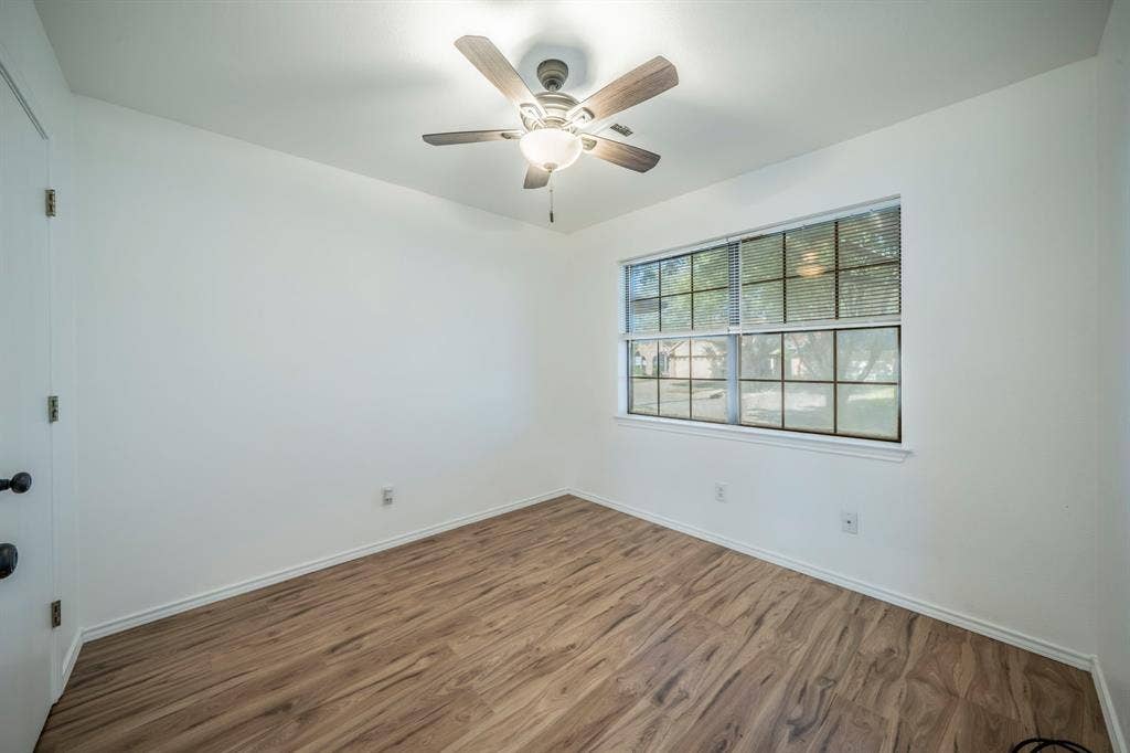 Room featuring wood-finish flooring, a multi-pane window, and a ceiling fan with integrated lighting