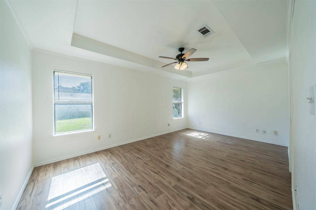 Primary featuring a tray ceiling, wood-finish flooring, dual windows, and a ceiling fan with integrated lighting