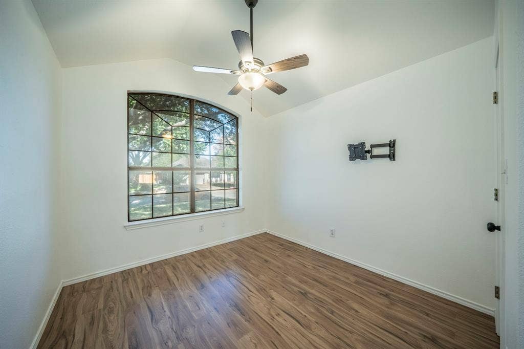 Vaulted ceiling room featuring wood-finish flooring, a multi-pane arched window, and a central ceiling fan with an integrated light fixture