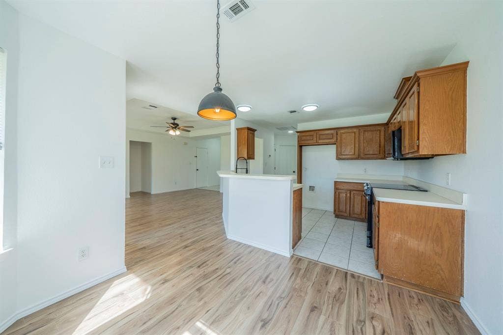 Kitchen featuring wood-finish cabinetry, tile flooring, a breakfast bar, and a dome pendant light, complemented by wood-finish flooring throughout the common area