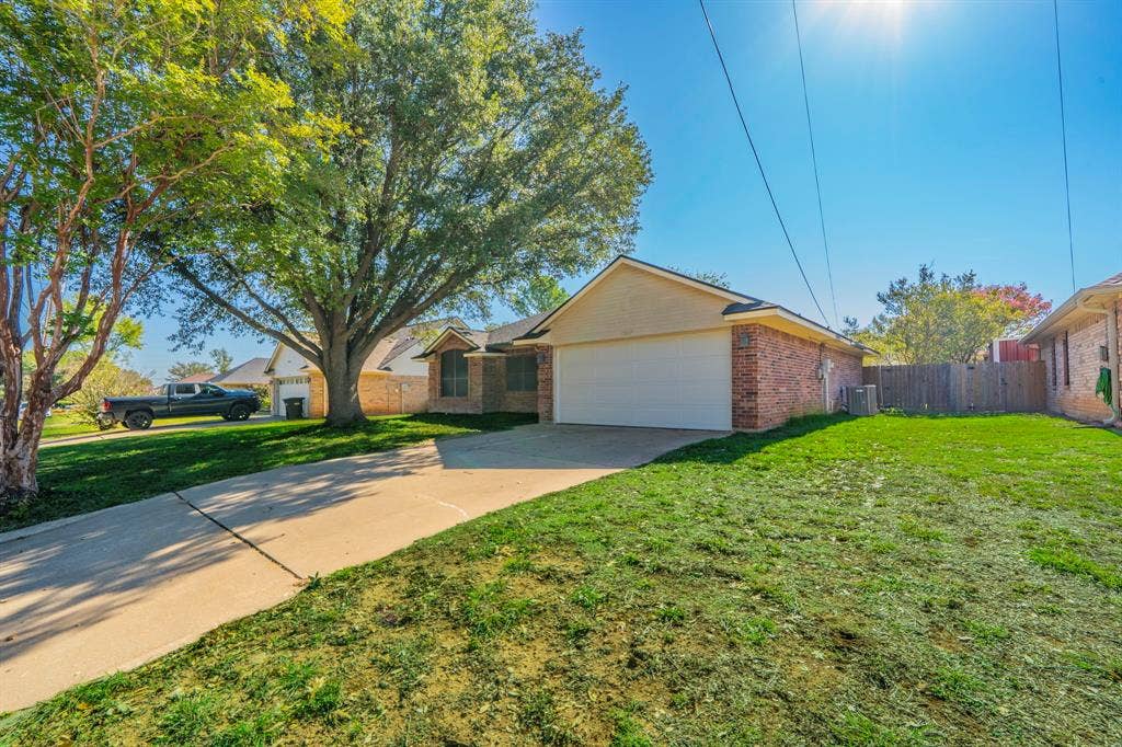 Single-story residence with a brick and stucco exterior, featuring an attached two-car garage, concrete driveway, and mature trees on the lot