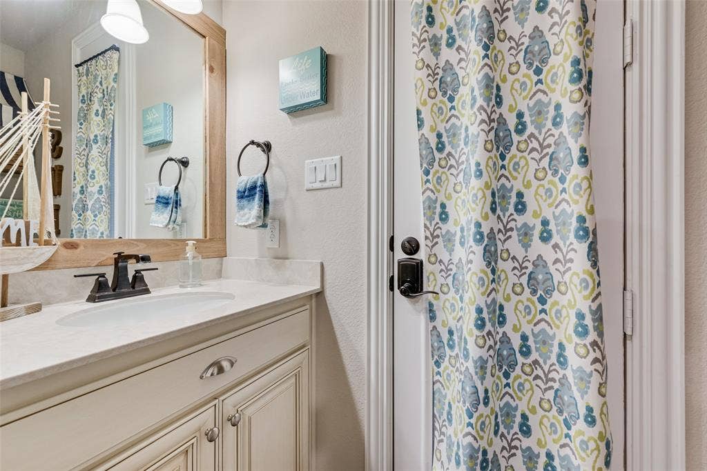 7231 Judy Drive, Ovilla, TX 75154 Vanity featuring light-toned cabinetry, a stone-finish countertop with an integrated oval basin, a dark-finish faucet, and a custom wood-framed mirror