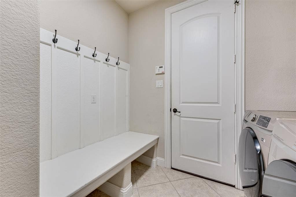 7231 Judy Drive, Ovilla, TX 75154 Built-in white board-and-batten mudroom bench featuring black hardware hooks, arched-top interior door, and ceramic tile flooring