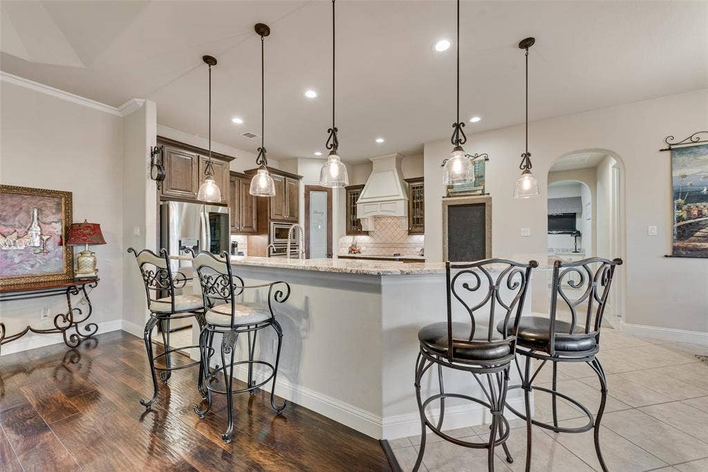 7231 Judy Drive, Ovilla, TX 75154 Kitchen featuring a tiered stone-surface island, wood-finish cabinetry, a decorative stove hood, recessed lighting, and glass pendant fixtures