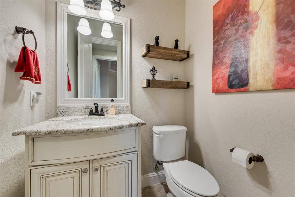 7231 Judy Drive, Ovilla, TX 75154 Curved cabinetry with stone countertop, undermount sink, multi-light fixture, framed wall mirror, and floating wood shelving