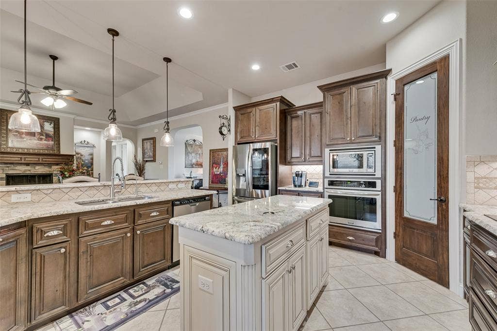 7231 Judy Drive, Ovilla, TX 75154 Kitchen featuring stained wood cabinetry, stone-finish countertops, a center island with a contrasting finish, stainless steel built-in double wall ovens, and a pantry door with decorative glass paneling
