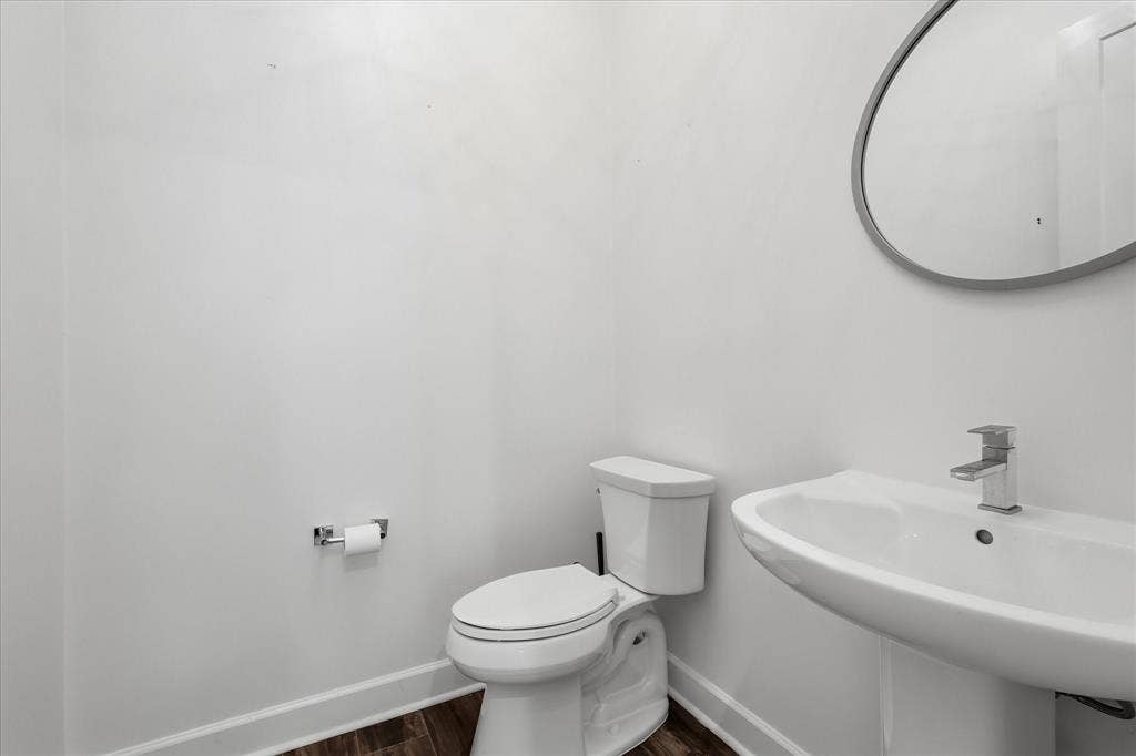 1813 Park Avenue, #106, Dallas, TX 75215 Pedestal sink with a single-handle faucet, oval wall-mounted mirror with a metallic frame, and wood-finish flooring