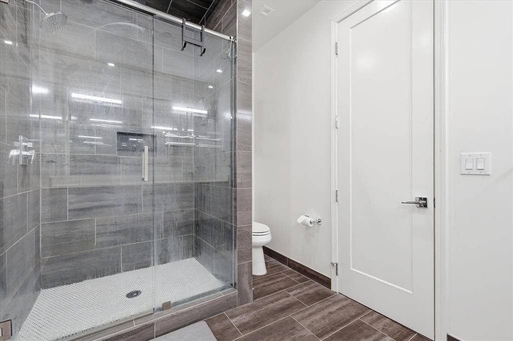 1813 Park Avenue, #106, Dallas, TX 75215 Walk-in shower featuring glass enclosure, large-format grey wall tile, built-in recessed wall niche, and textured tile floor, complemented by wood-finish floor tiling