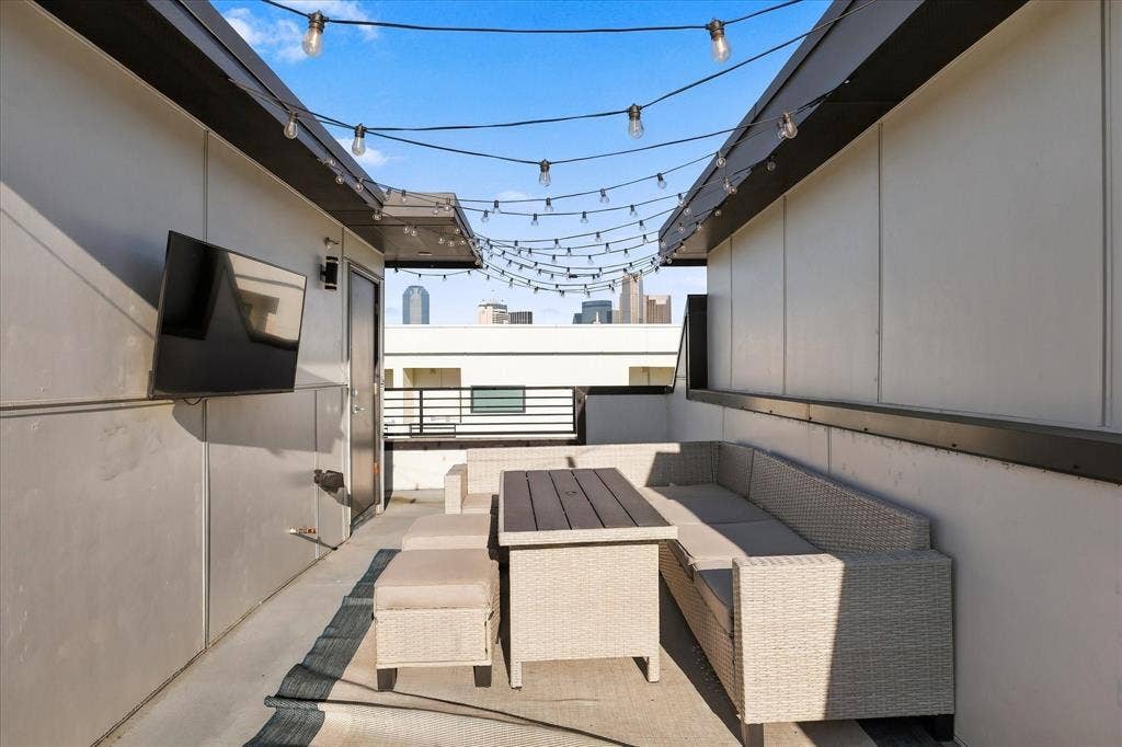 1813 Park Avenue, #106, Dallas, TX 75215 Rooftop terrace featuring concrete flooring, perimeter wall-mounted string lighting, metal railing, and city skyline backdrop