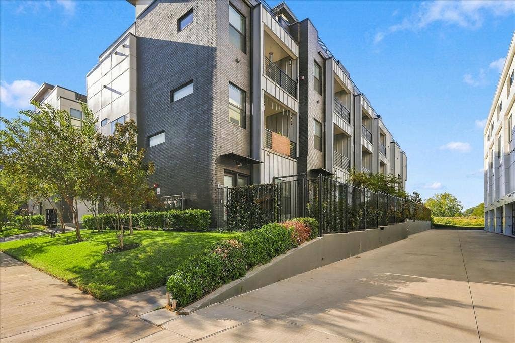 1813 Park Avenue, #106, Dallas, TX 75215 Modern multi-story exterior featuring dark brick masonry, vertical metal siding, recessed balconies with metal railings, and a tiered landscaped border