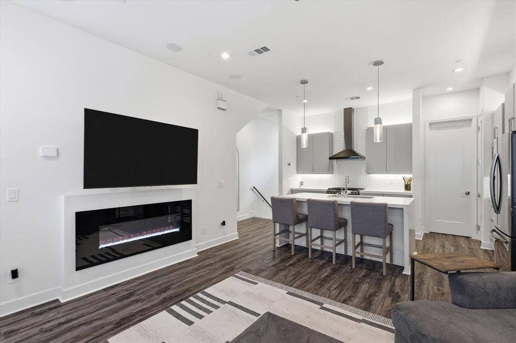 1813 Park Avenue, #106, Dallas, TX 75215 Linear wall-mounted electric fireplace, wood-finish flooring, kitchen island with stone countertop, stainless steel range hood, and pendant lighting