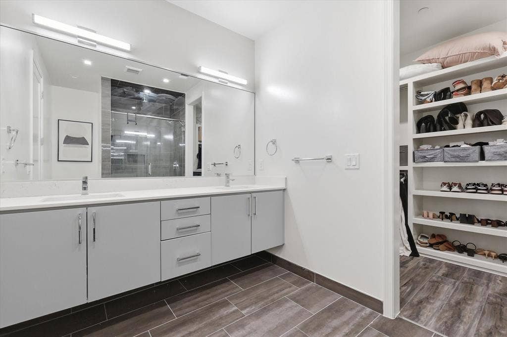 1813 Park Avenue, #106, Dallas, TX 75215 Floating dual-sink vanity with light gray cabinetry and white countertop, full-width wall mirror, wood-finish flooring, and walk-in closet featuring custom built-in shelving