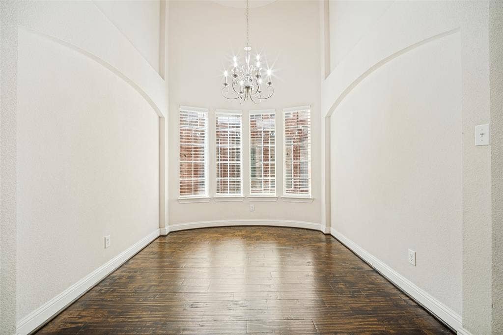 Vaulted ceilings featuring an arched architectural detail, multi-pane bay windows, wood-finish flooring, and a tiered chandelier