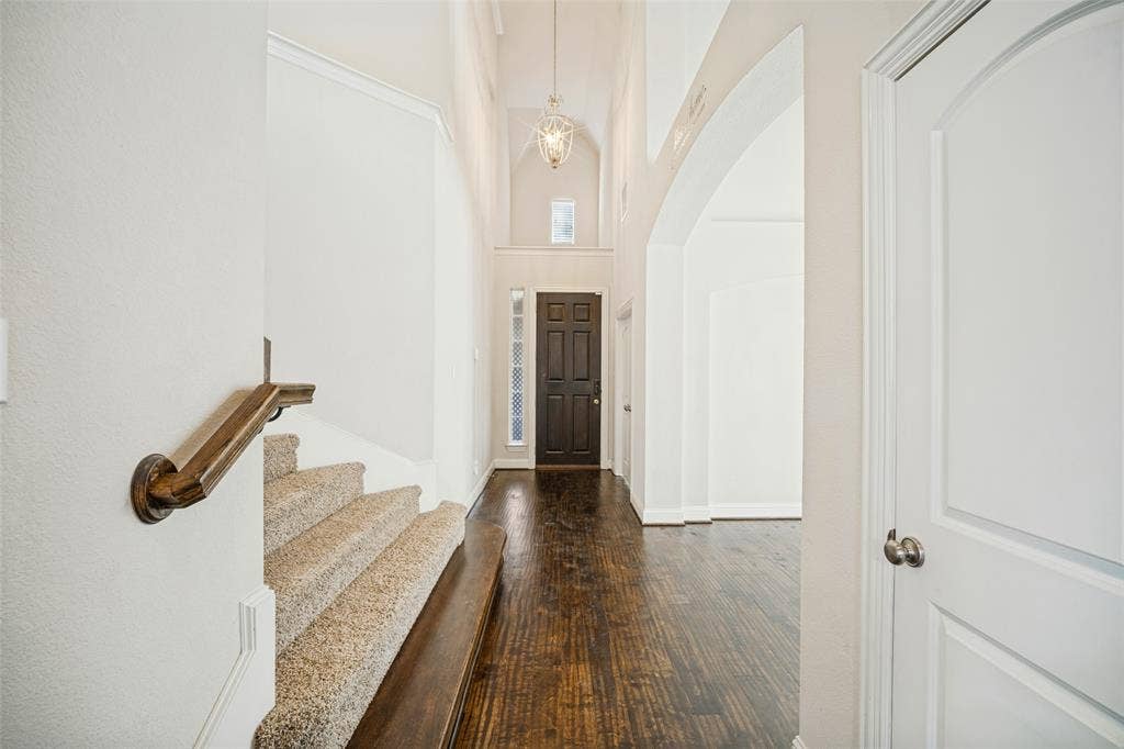 Foyer featuring vaulted ceilings, dark wood-finish flooring, a decorative pendant light fixture, carpeted staircase with a wood handrail, and an arched entryway
