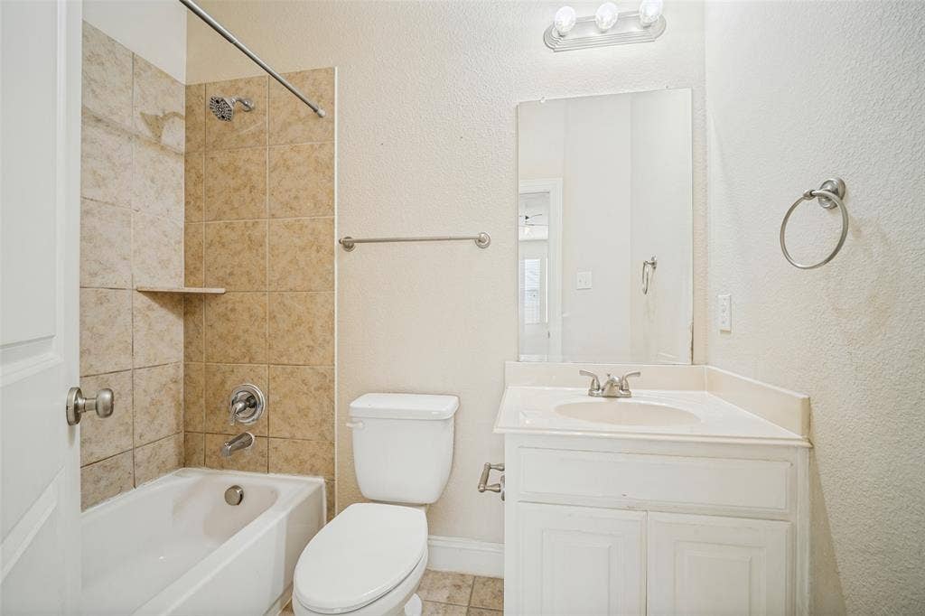Bathroom featuring a vanity with integrated sink, chrome hardware, neutral ceramic wall tiling in the shower area, and a wall-mounted light fixture