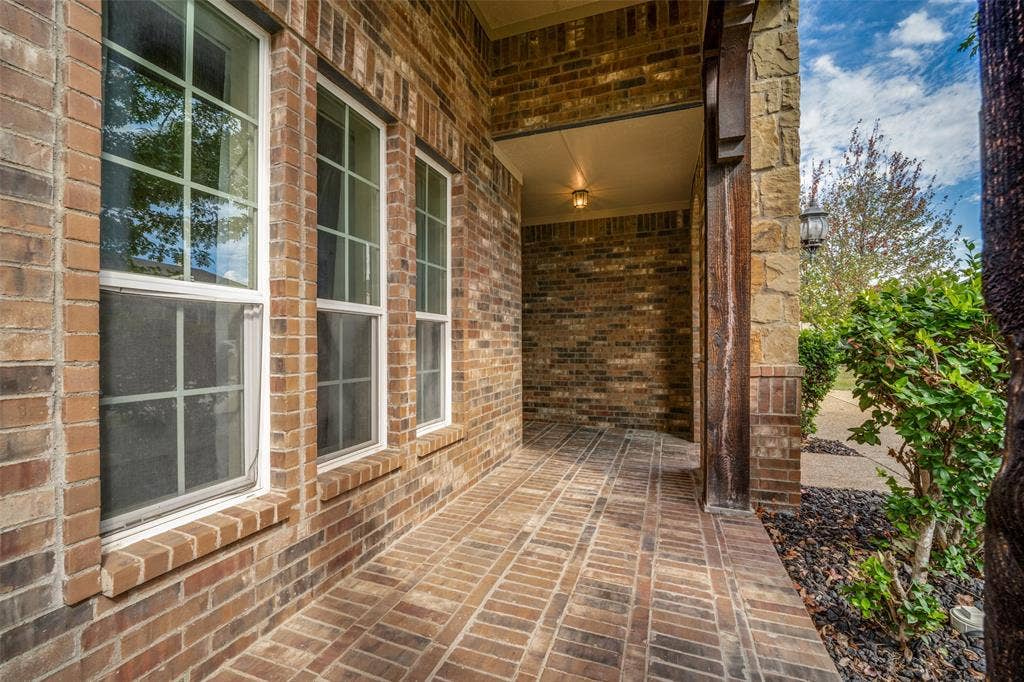 Covered entryway featuring brick masonry construction, grid-patterned windows, herringbone-laid brick flooring, and a stone-clad column