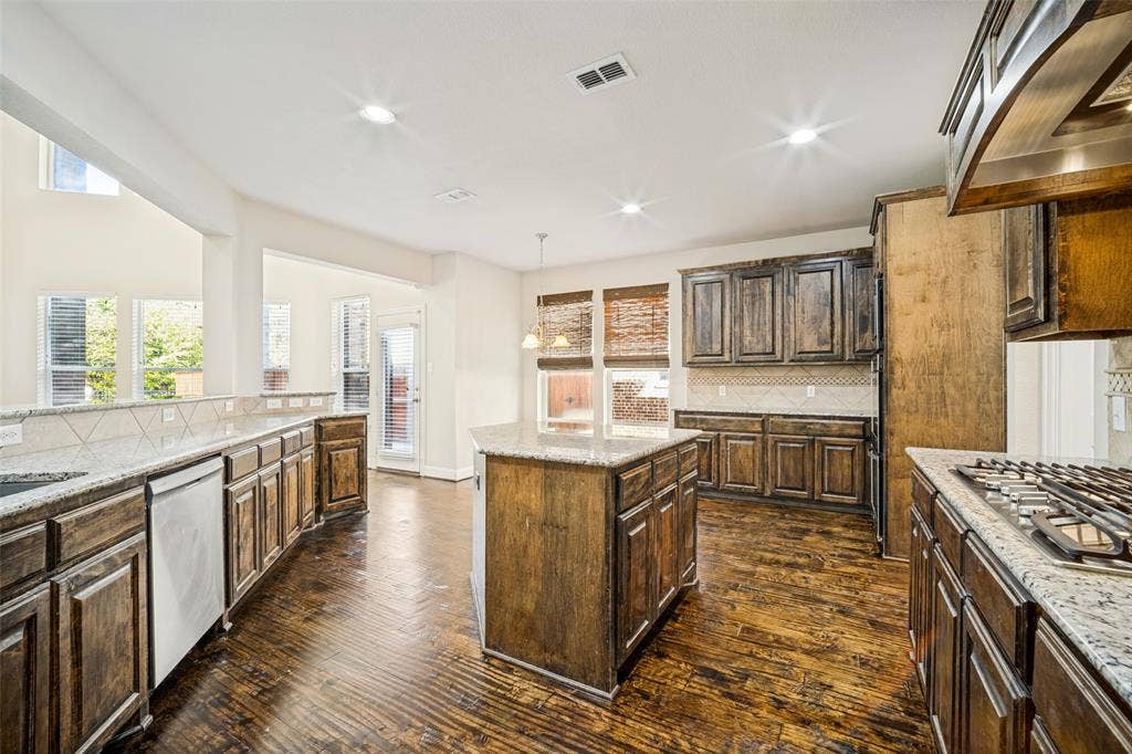 Kitchen featuring custom stained wood cabinetry, stone-surface countertops, central island, wood-finish flooring, and built-in stainless steel gas cooktop