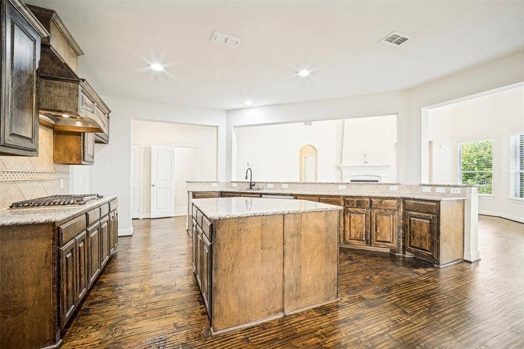 Kitchen featuring dark wood-finish cabinetry, granite countertops, a central island, a custom vent hood, and wood-finish flooring