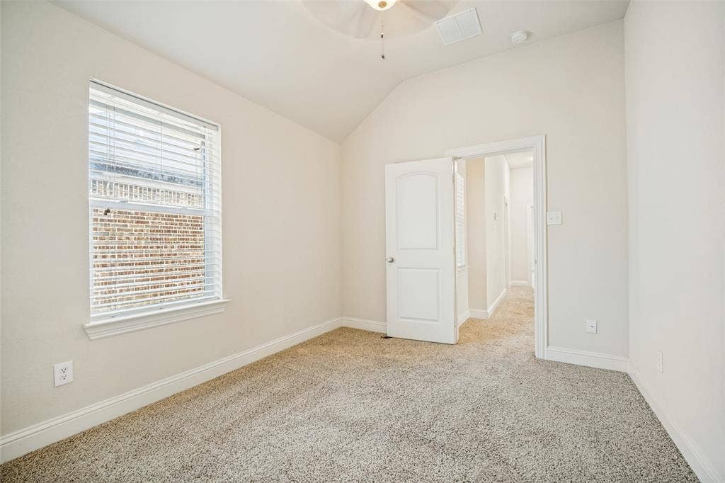 Room featuring vaulted ceilings, neutral carpeting, a multi-pane window with adjustable blinds, and an integrated ceiling fan