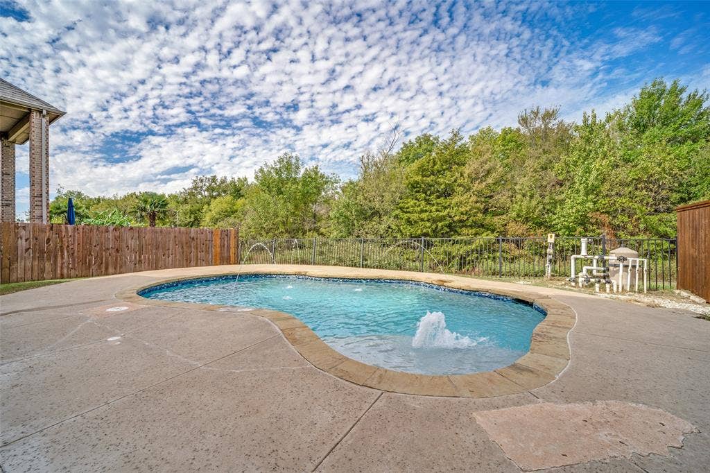 In-ground pool featuring a stamped concrete deck, multiple water jets, and perimeter metal fencing