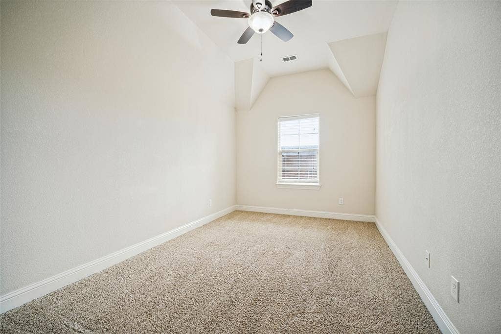 Room featuring a vaulted ceiling, neutral wall coloring, carpeted flooring, a single window with blinds, and an integrated ceiling fan
