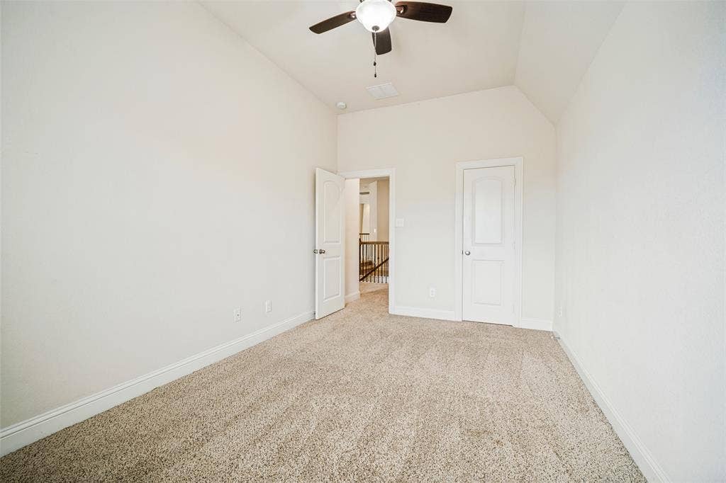Vaulted ceiling featuring a central ceiling fan with integrated lighting, neutral wall-to-wall carpeting, and two interior doors with molded panel detailing