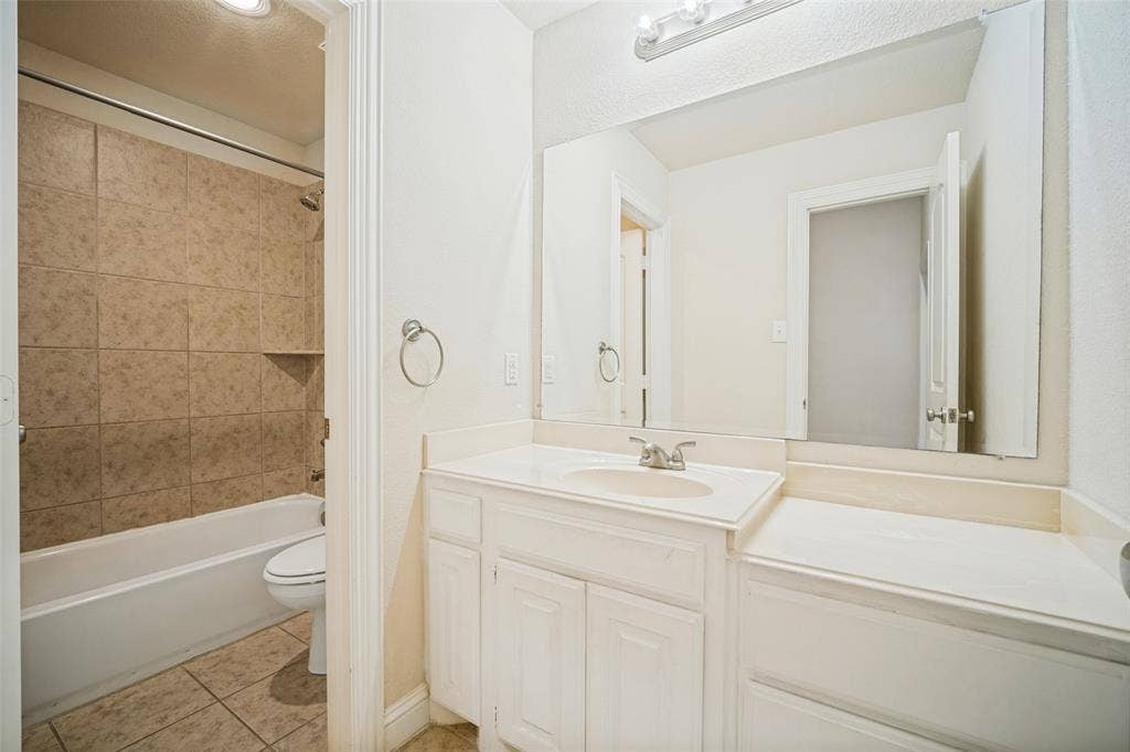 Bathroom featuring a white vanity with an integrated countertop, large wall-mounted mirror, three-light fixture, and a tile-surround shower and tub combination