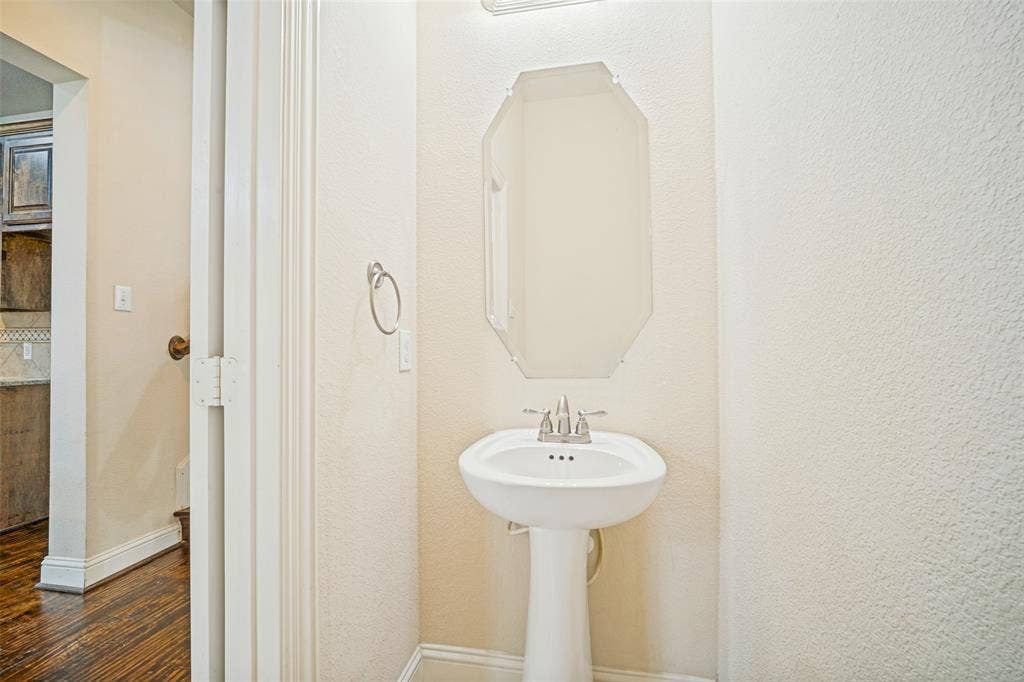 White porcelain pedestal sink, polished chrome widespread faucet, octagonal wall-mounted mirror, and wood-finish flooring