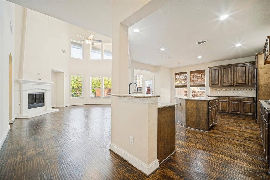 High-ceiling interior featuring dark-stained wood cabinetry, stone-finish countertops, wood-finish flooring, and a fireplace with a decorative mantel