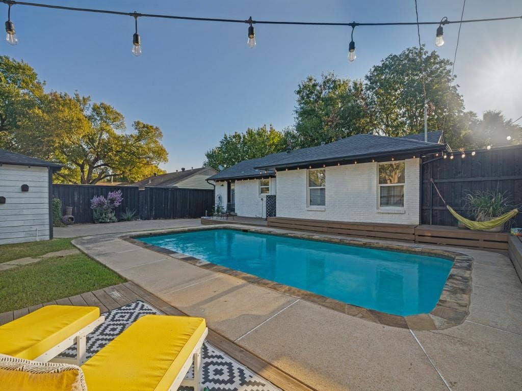 200 S Weatherred Drive, Richardson, TX 75080 In-ground swimming pool with stone coping, white painted brick exterior, stained wood decking, and dark wood privacy fencing